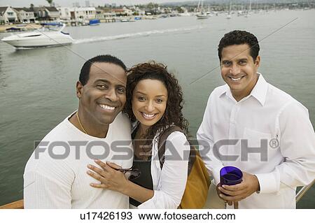 Stock Image - Couple with friend on yacht, (portrait), (elevated view). Fotosearch