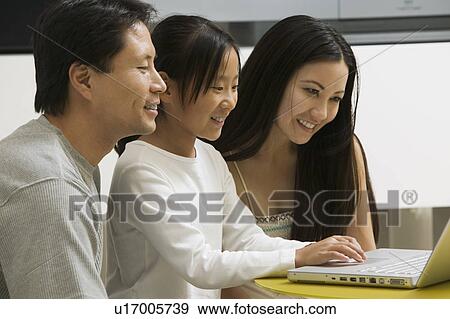 Stock Photo - Daughter using laptop with mother and father in living room. Fotosearch