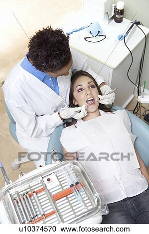 Stock Image - Dentist examining patient in surgery. Fotosearch