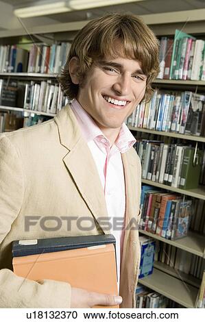 Stock Image - Elegant college student in library, holding exercise books.. Fotosearch