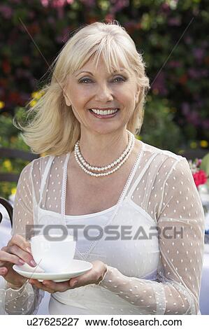 Stock Photo - Elegant middle aged woman holding cup of tea outdoors. Fotosearch