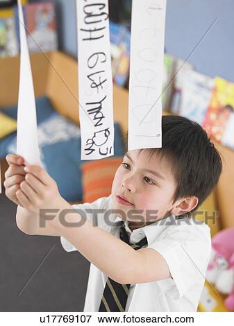Stock Photo - Elementary schoolboy learning to read from hanging paper strip in classroom, elevated view. Fotosearch
