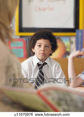 Stock Photograph - Elementary schoolboy listening to teacher read in classroom. Fotosearch