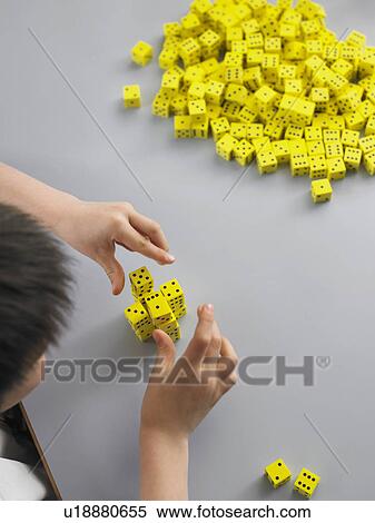 Stock Photography - Elementary schoolboy playing with dice on desk, elevated view. Fotosearch