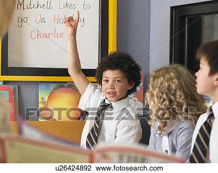 Stock Image - Elementary schoolboy raising hand in classroom. Fotosearch