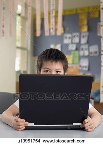 Elementary schoolboy sitting behind opened laptop in classroom View Large Photo Image Picture - Elementary schoolboy sitting behind opened laptop in classroom. Fotosearch