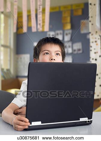 Elementary schoolboy sitting behind opened laptop in classroom View Large Photo Image Stock Image - Elementary schoolboy sitting behind opened laptop in classroom. Fotosearch