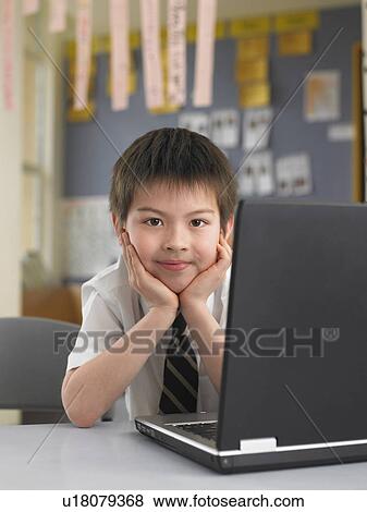 Stock Photo - Elementary schoolboy sitting by laptop in classroom. Fotosearch