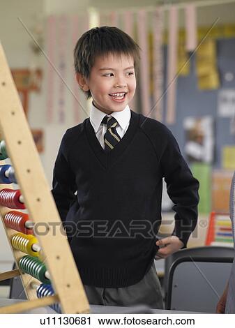 Stock Image - Elementary schoolboy standing by abacus in classroom. Fotosearch