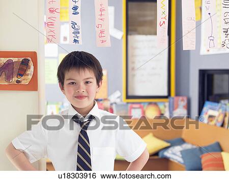 Stock Photograph - Elementary schoolboy standing in classroom, portrait. Fotosearch