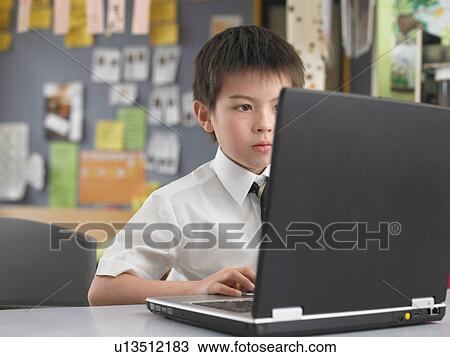 Stock Image - Elementary schoolboy using laptop in classroom. Fotosearch