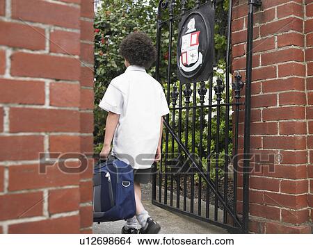 Picture - Elementary schoolboy walking through school gate, back view. Fotosearch