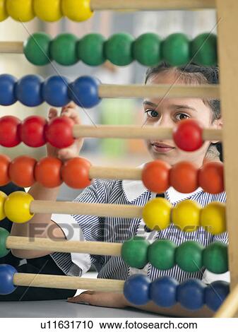 Stock Image - Elementary schoolgirl looking through abacus, sitting in classroom. Fotosearch