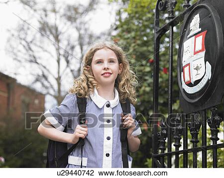 Stock Image - Elementary schoolgirl standing by school gate. Fotosearch