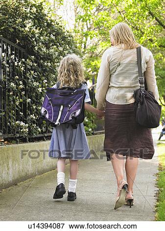 Elementary schoolgirl walking with mother on pavement, back view View Large Photo Image Stock Photo - Elementary schoolgirl walking with mother on pavement, back view. Fotosearch