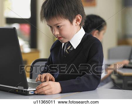 Stock Image - Elementary student using laptop in classroom. Fotosearch