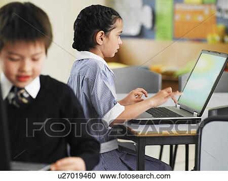 Stock Image - Elementary students using laptops in classroom. Fotosearch