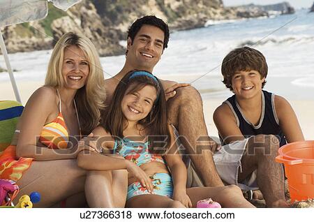 Stock Photo - Family in swimwear sitting on beach, portrait. Fotosearch