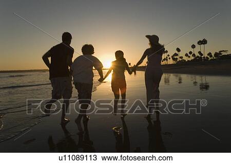 Stock Image - Family running through sea at sunset, back view, silhouette. Fotosearch