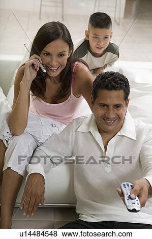 Family sitting on sofa watching TV, mother on mobile phone View Large Photo Image Stock Photo - Family sitting on sofa watching TV, mother on mobile phone. Fotosearch