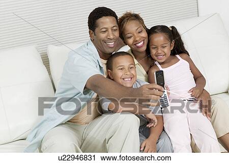 Stock Image - Family Taking Picture of family on sofa with Camera Phone. Fotosearch