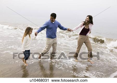 Stock Image - Family walking through surf on beach. Fotosearch