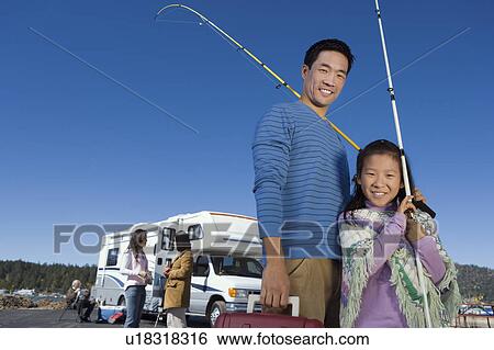 Stock Photograph - Father and daughter holding fishing poles outside RV. Fotosearch