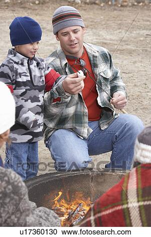 Stock Image - Father and son (7-9) by campfire. Fotosearch