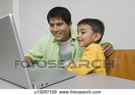 Stock Photo - Father and Son at desk Using Laptop, close up. Fotosearch