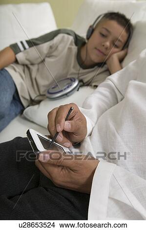 Picture - Father Using PDA on sofa with Son Listening to Music, close up of hands of father. Fotosearch