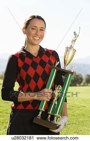 Stock Image - Female golfer holding trophy, (portrait). Fotosearch
