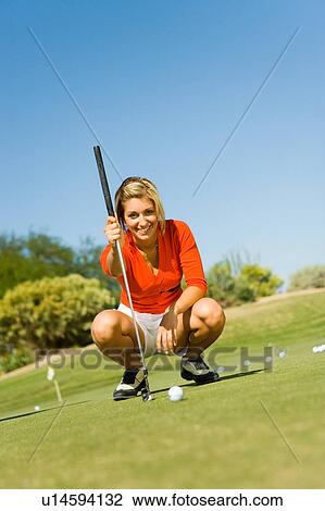 Stock Image - Female golfer lining up shot on putting green. Fotosearch