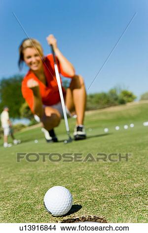 Female golfer looking at ball rolling towards cup, focus on ball View Large Photo Image Picture - Female golfer looking at ball rolling towards cup, focus on ball. Fotosearch