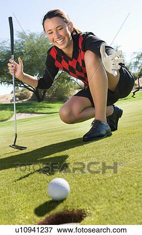 Stock Photo - Female golfer looking at ball rolling towards cup. Fotosearch
