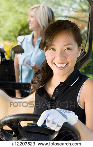 Stock Image - Female golfer sitting in golf cart. Fotosearch
