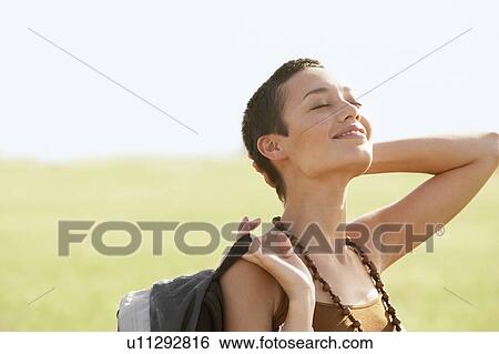 Stock Photograph - Female hiker basking in sun, standing in field. Fotosearch