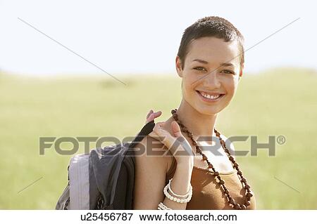 Stock Photo - Female hiker holding backpack, standing in field, portrait. Fotosearch