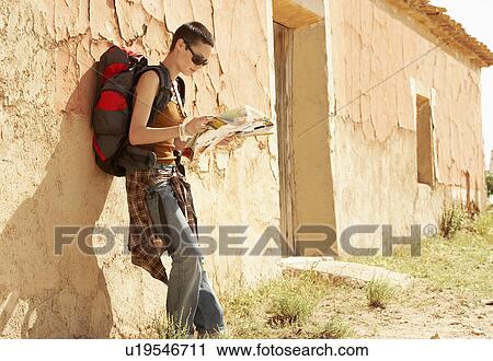 Stock Image - Female hiker reading map by desolate farmhouse. Fotosearch