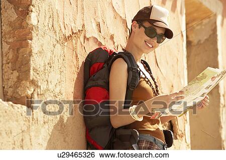 Stock Photograph - Female hiker reading map leaning on dilapidated house. Fotosearch