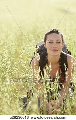 Stock Photograph - Female hiker squatting in long grass, portrait. Fotosearch