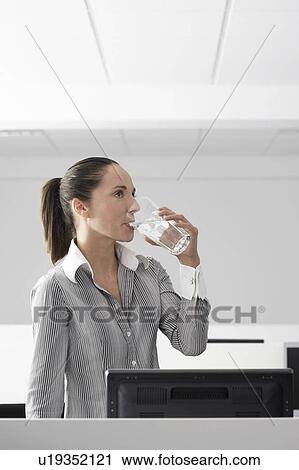 Female office worker drinking water in office cubicle View Large Photo Image Stock Image - Female office worker drinking water in office cubicle. Fotosearch