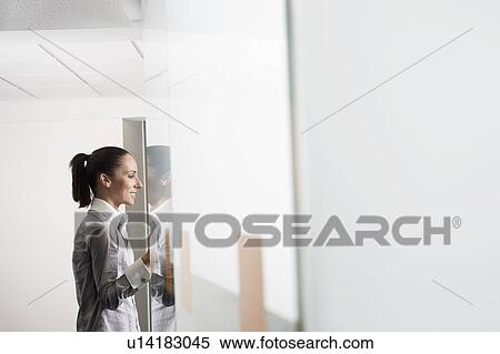 Stock Photography - Female office worker standing in office doorway, side view. Fotosearch