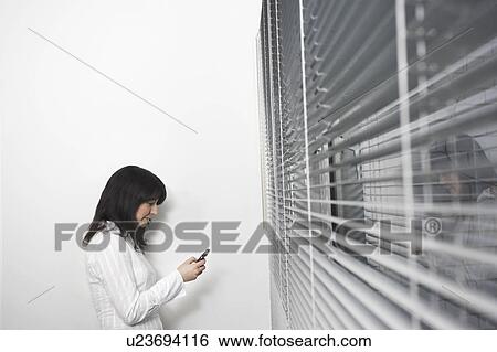 Stock Photograph - Female office worker using mobile phone in front of office window, side view. Fotosearch