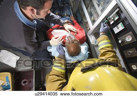 Stock Photography - Firefighter and paramedic helping man in ambulance. Fotosearch