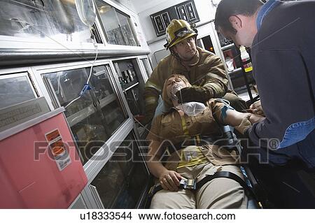 Picture - Firefighter and paramedic helping woman in ambulance. Fotosearch