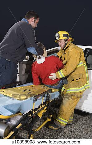 Stock Photo - Firefighter and paramedic rescuing car accident victim. Fotosearch