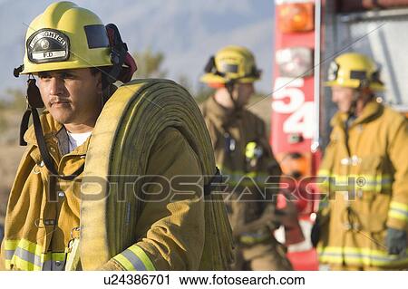 Stock Image - Firefighter carrying hose. Fotosearch