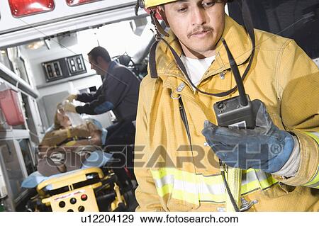 Stock Photo - Firefighter using radio, paramedic tending victim. Fotosearch