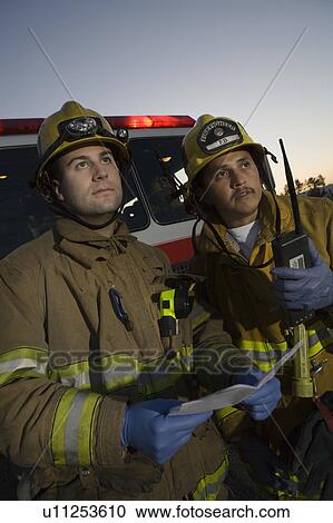 Stock Image - Firefighters planning rescue by fire engine. Fotosearch