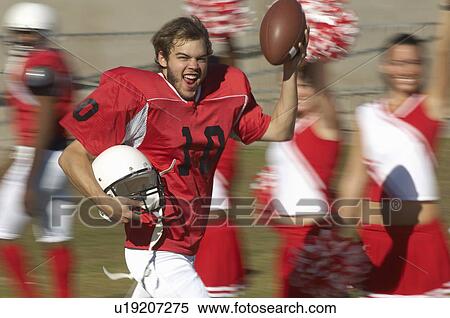 Stock Photography - Football player holding ball running by cheerleaders. Fotosearch